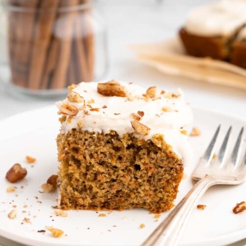 A piece of healthy carrot cake with healthy cream cheese frosting on a white plate with a fork on the side