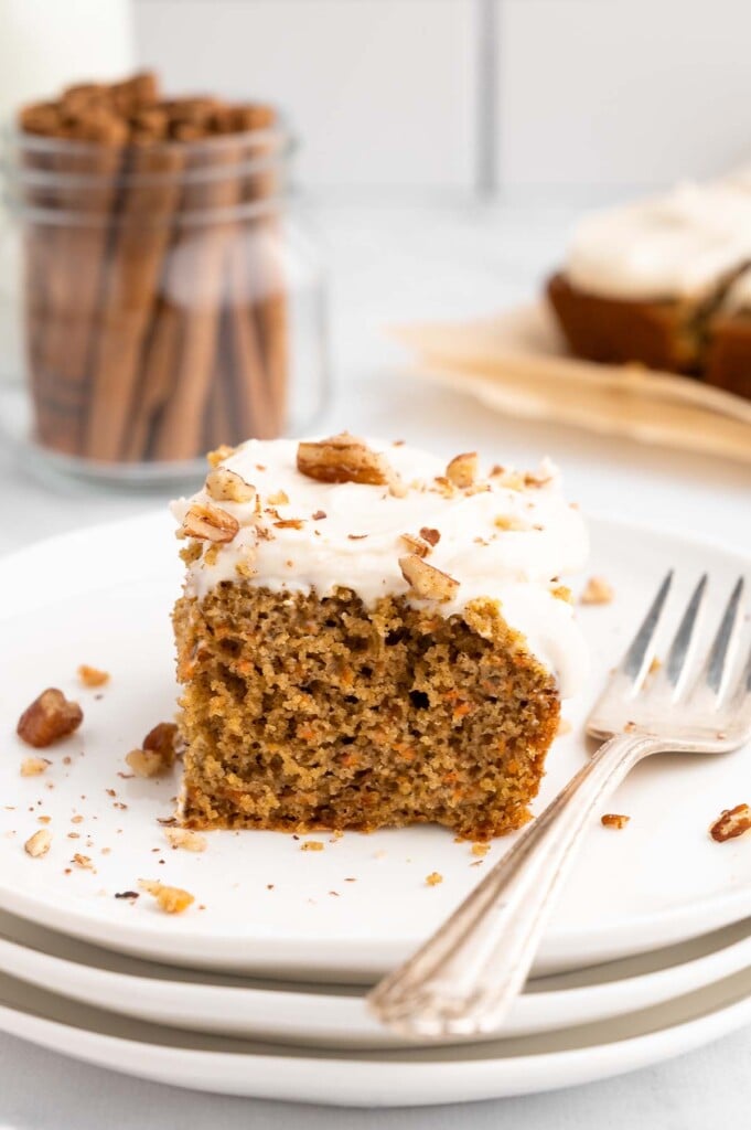 A piece of healthy carrot cake with healthy cream cheese frosting on a white plate with a fork on the side