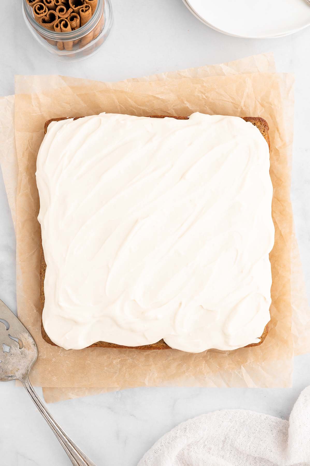 An overhead shot of a freshly frosted healthy carrot cake with healthy cream cheese frosting on parchment paper