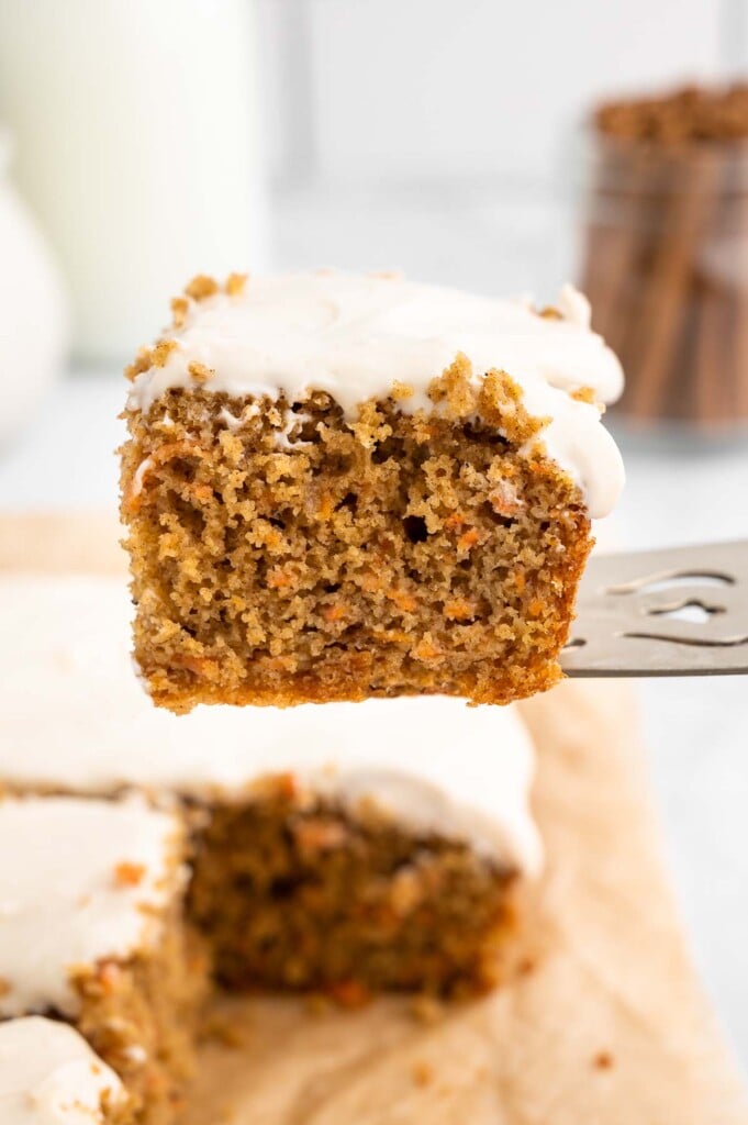 A silver spatula lifting a piece of healthy carrot cake away from a full cake
