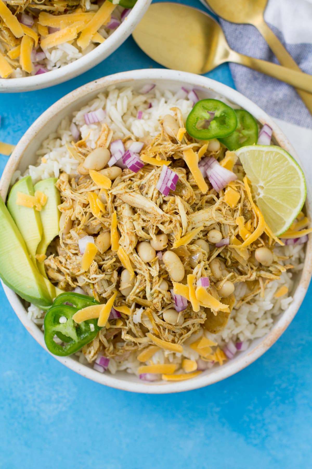 A close up of healthy chicken chili in a white bowl on a bright blue background
