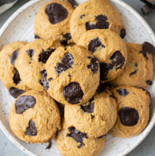 A close up of Healthy Chocolate Chip Cookies on a white plate with a linen and cookie sheet off to the side