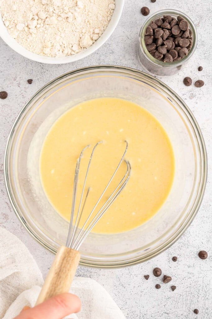 Wet ingredients for healthy chocolate chip muffins in a glass bowl with a whisk in the bowl.