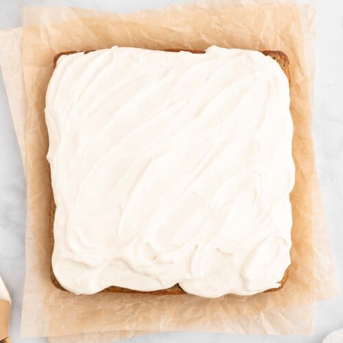An overhead shot of a healthy carrot cake frosted with a healthy cream cheese frosting on a piece of parchment paper