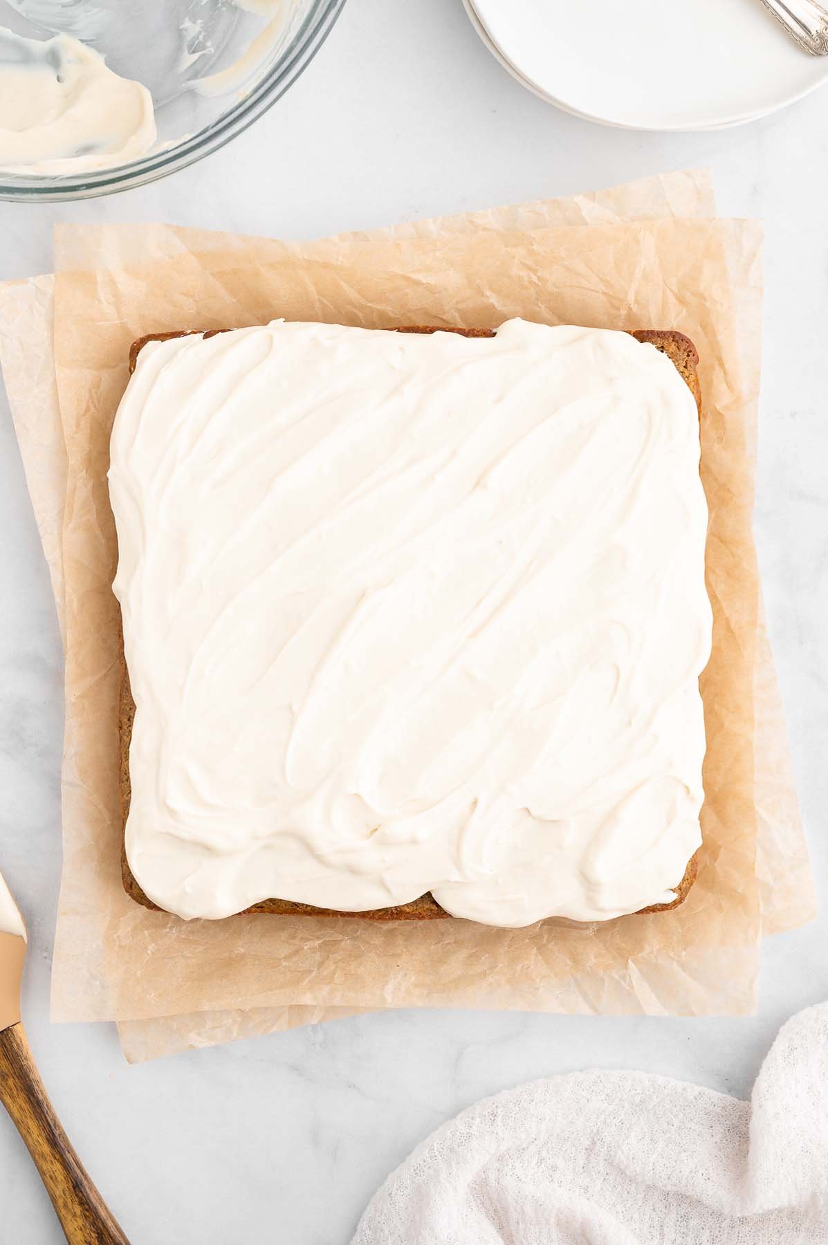 An overhead shot of a healthy carrot cake frosted with a healthy cream cheese frosting on a piece of parchment paper