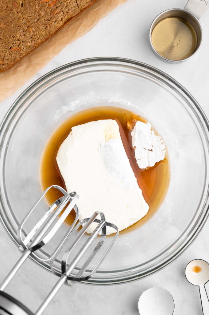 Ingredients for healthy cream cheese frosting in a clear bowl before being blended with beaters on the side