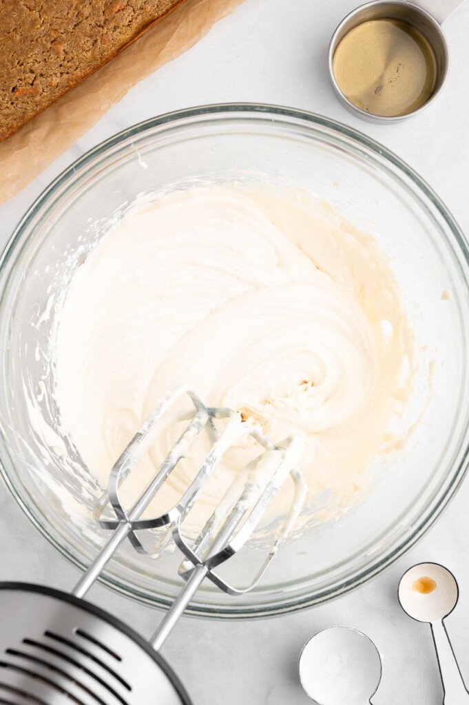 Healthy Cream Cheese Frosting being beat with beaters in a clear bowl on a white background
