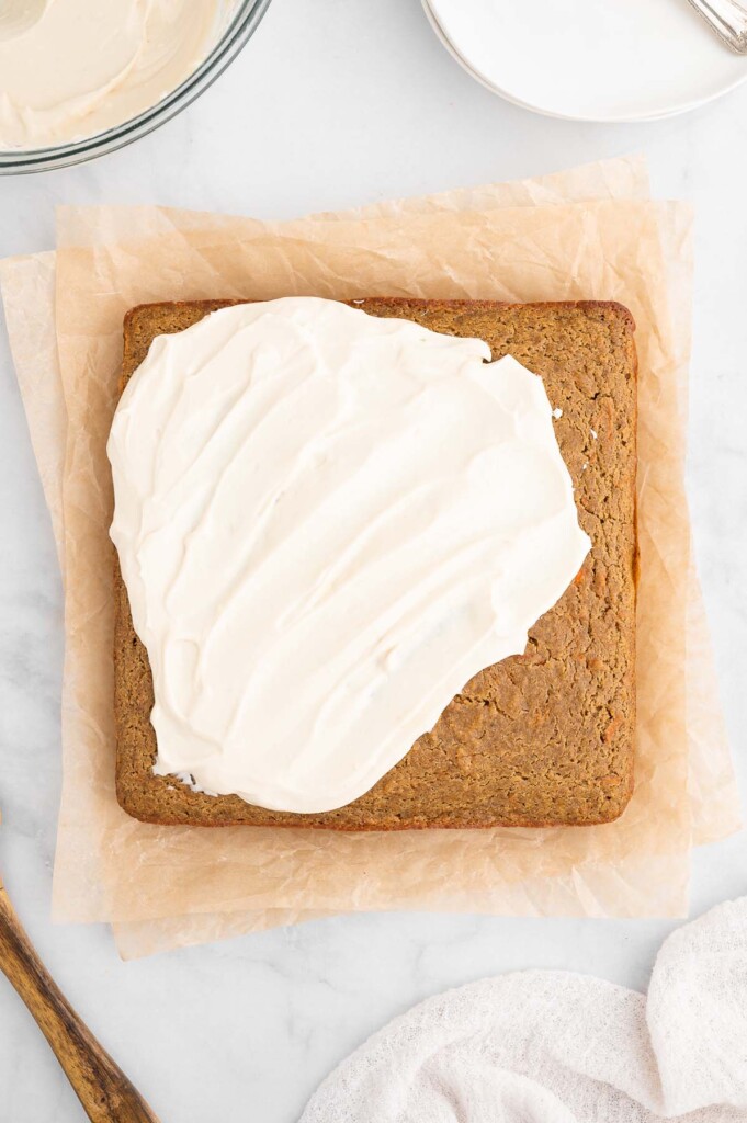 An overhead shot of a healthy carrot cake being frosted with a healthy cream cheese frosting on a piece of parchment paper