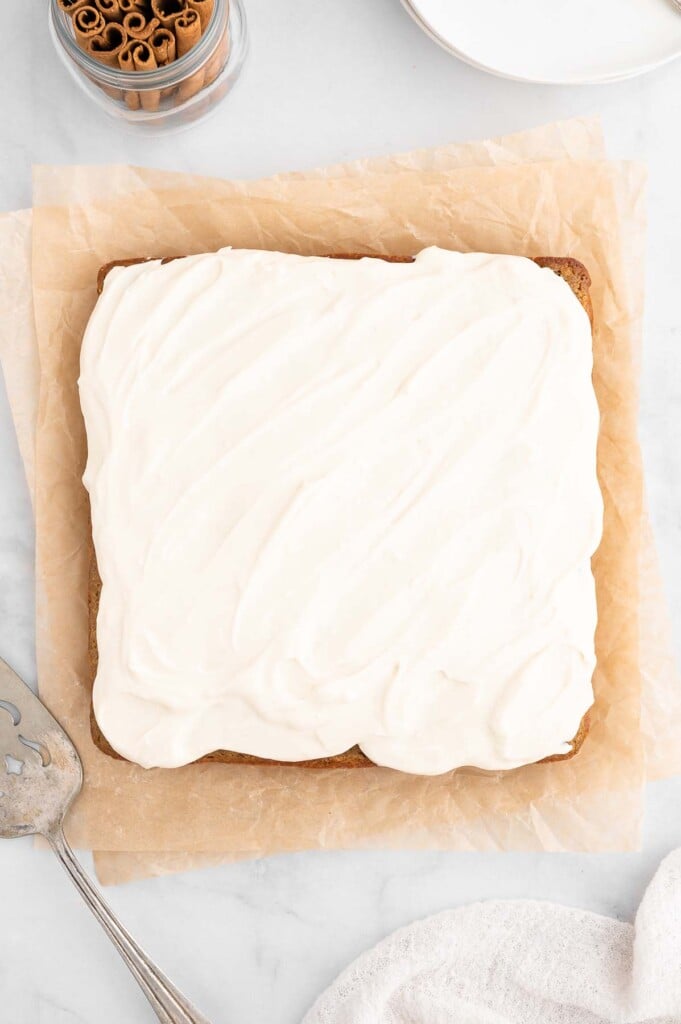 An overhead shot of a healthy carrot cake frosted with a healthy cream cheese frosting on a piece of parchment paper