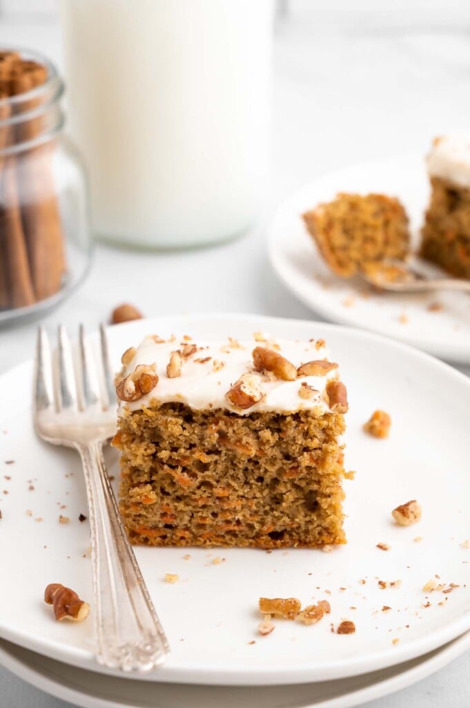 A piece of carrot cake with healthier cream cheese frosting with pecans and a fork on the side