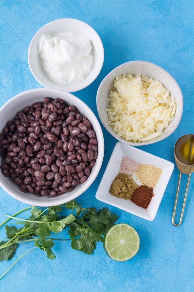 Ingredients for healthy bean dip in small white bowls on a bright blue background