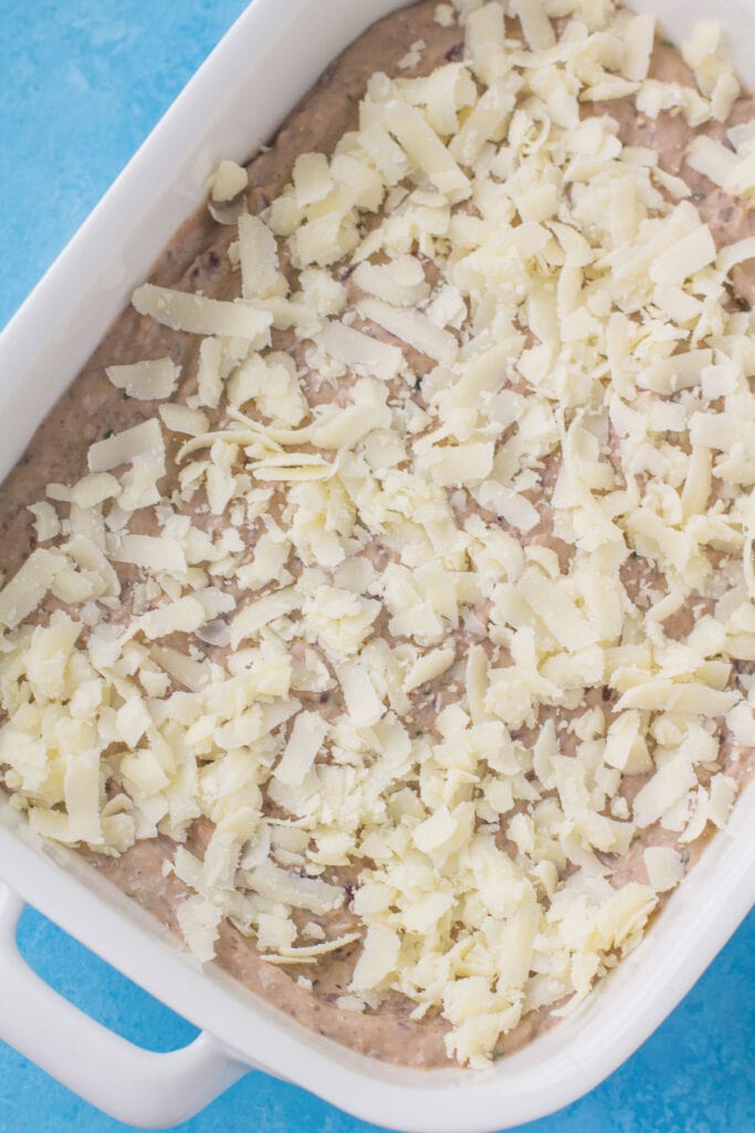a dish of easy dip being sprinkled with cheddar cheese before it goes into the oven.