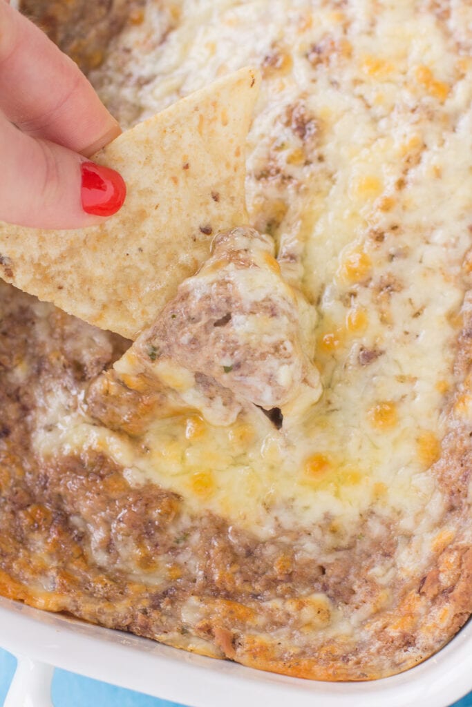 A chip scooping up a bite of the best healthy bean dip from a white dish
