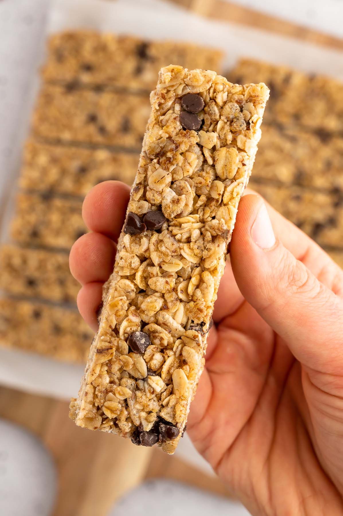 A hand holding up a single healthy homemade granola bar with more bars in the background