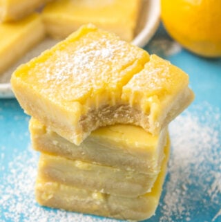 A close up of a stacked pile of lemon bars with a bite taken out of the one on top.