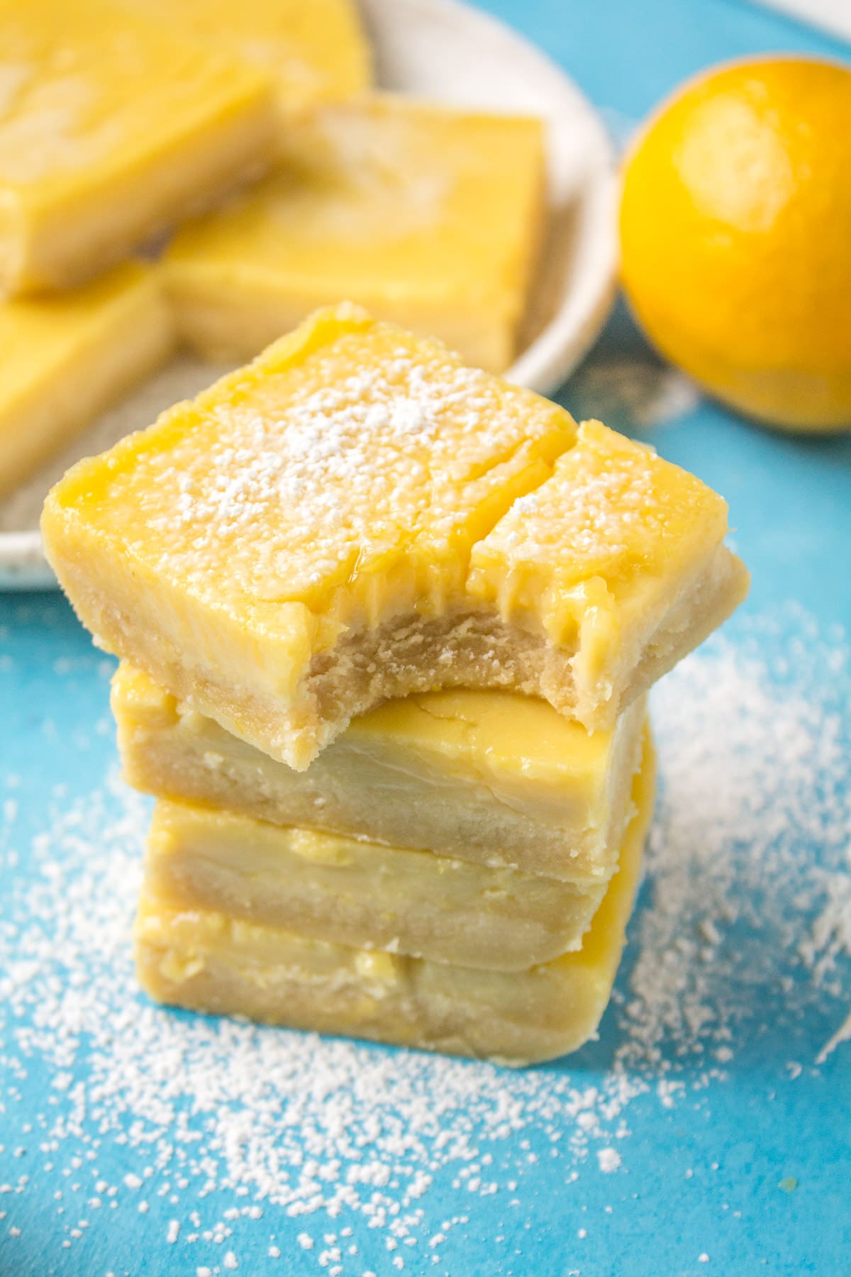 A close up of a stacked pile of lemon bars with a bite taken out of the one on top.