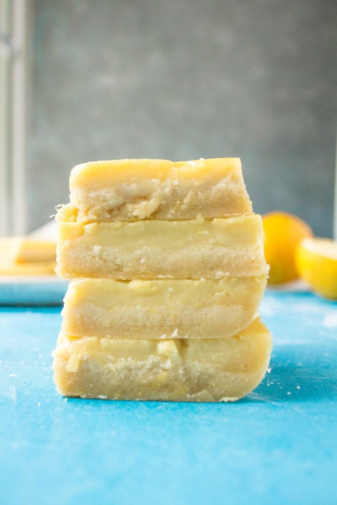 Healthy Lemon Bars stacked on a blue background with a grey background behind them. 