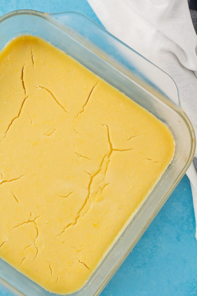 Healthy Lemon Bars in a glass baking dish on a bright blue background
