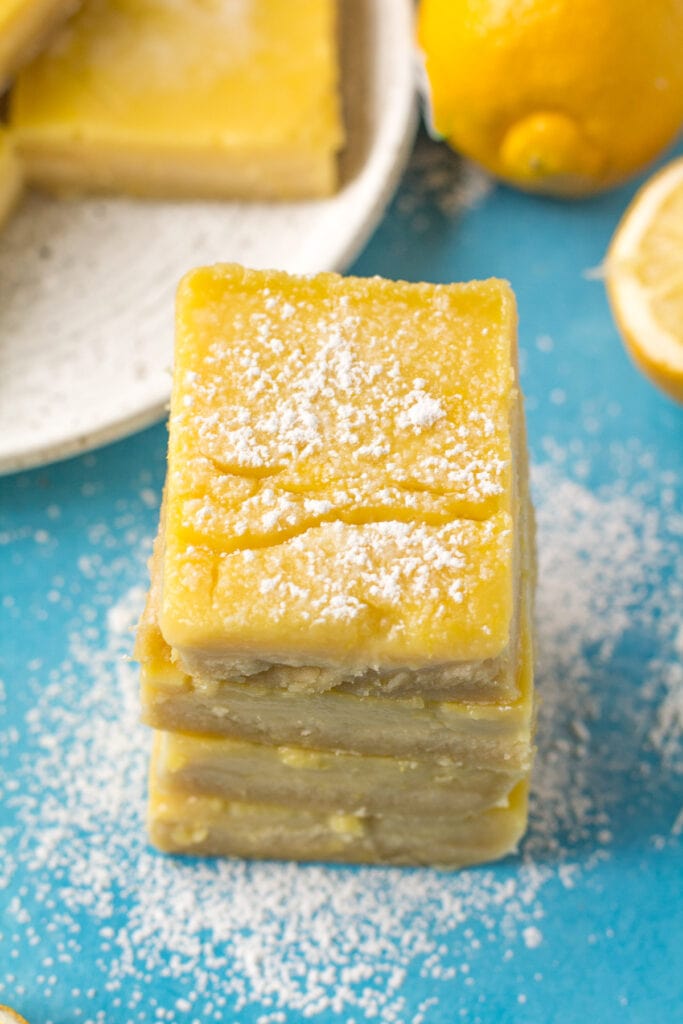 An overhead shot of Healthy Lemon Bars stacked with powdered sugar on a blue background