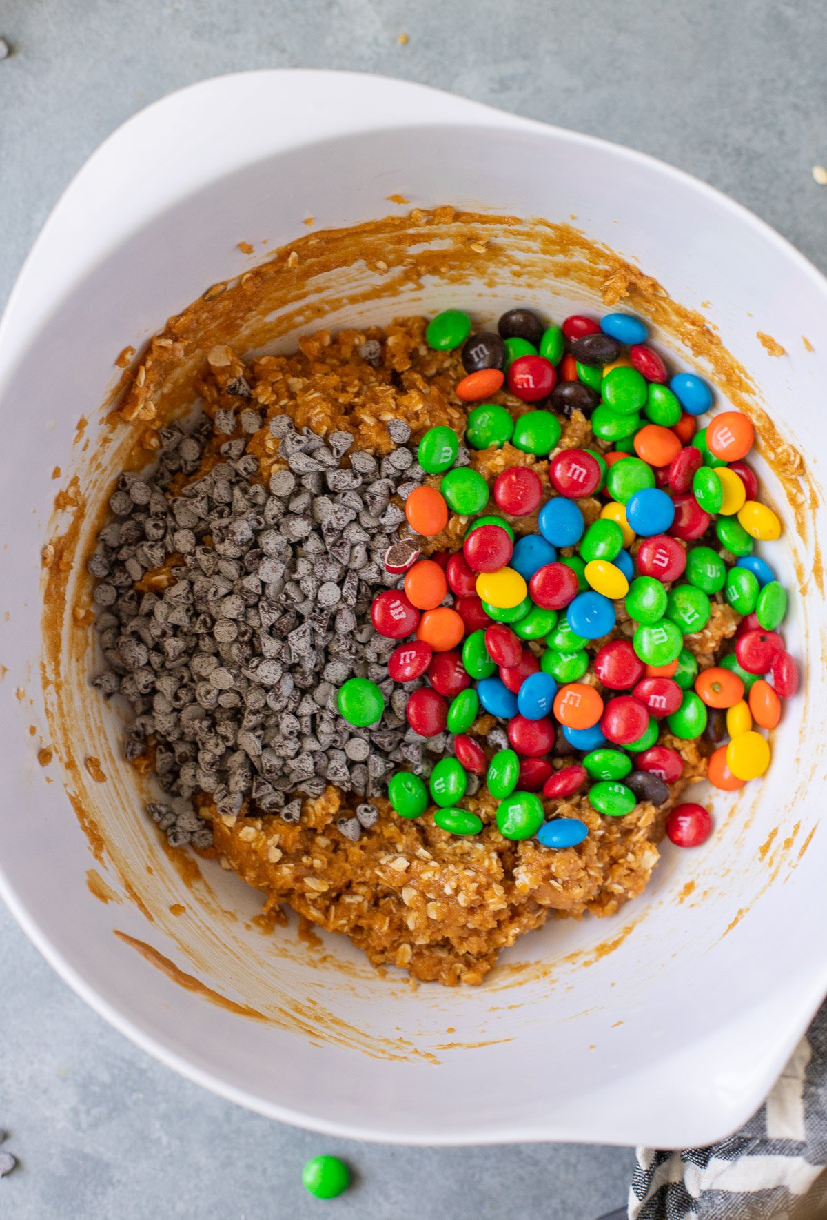 healthy monster cookie dough in a white bowl with chocolate chips and m&ms on top before being mixed in