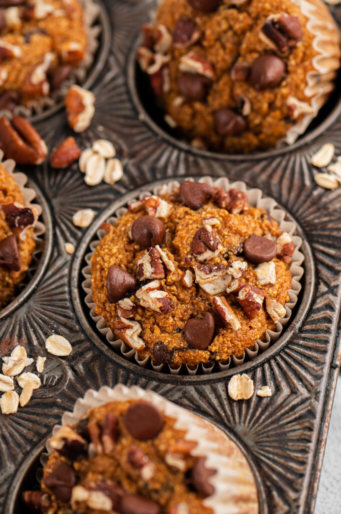 A sweet potato muffin in a muffin tin with nuts and oats on the edges
