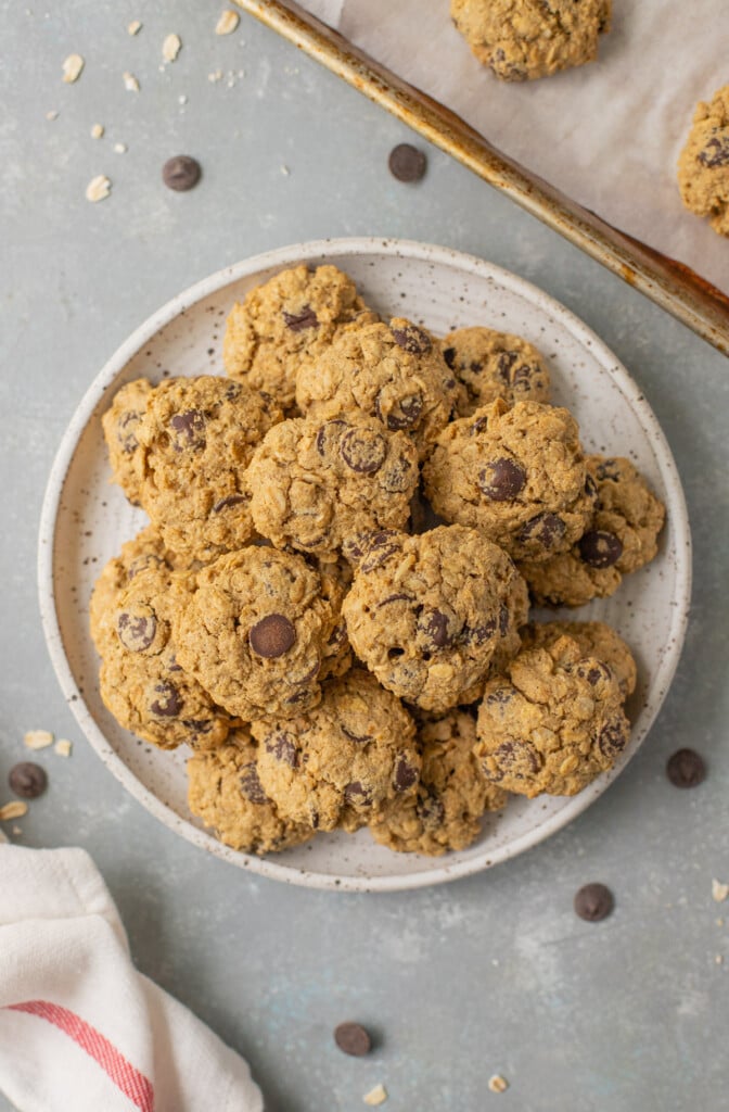 Healthy Oatmeal Chocolate Chip Cookies on a white plate on a grey counter with a baking sheet of cookies on the side