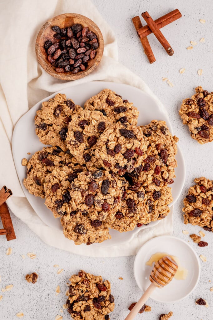 An overhead shot of a white plate of healthy oatmeal raisin cookies on a grey background with more cookies