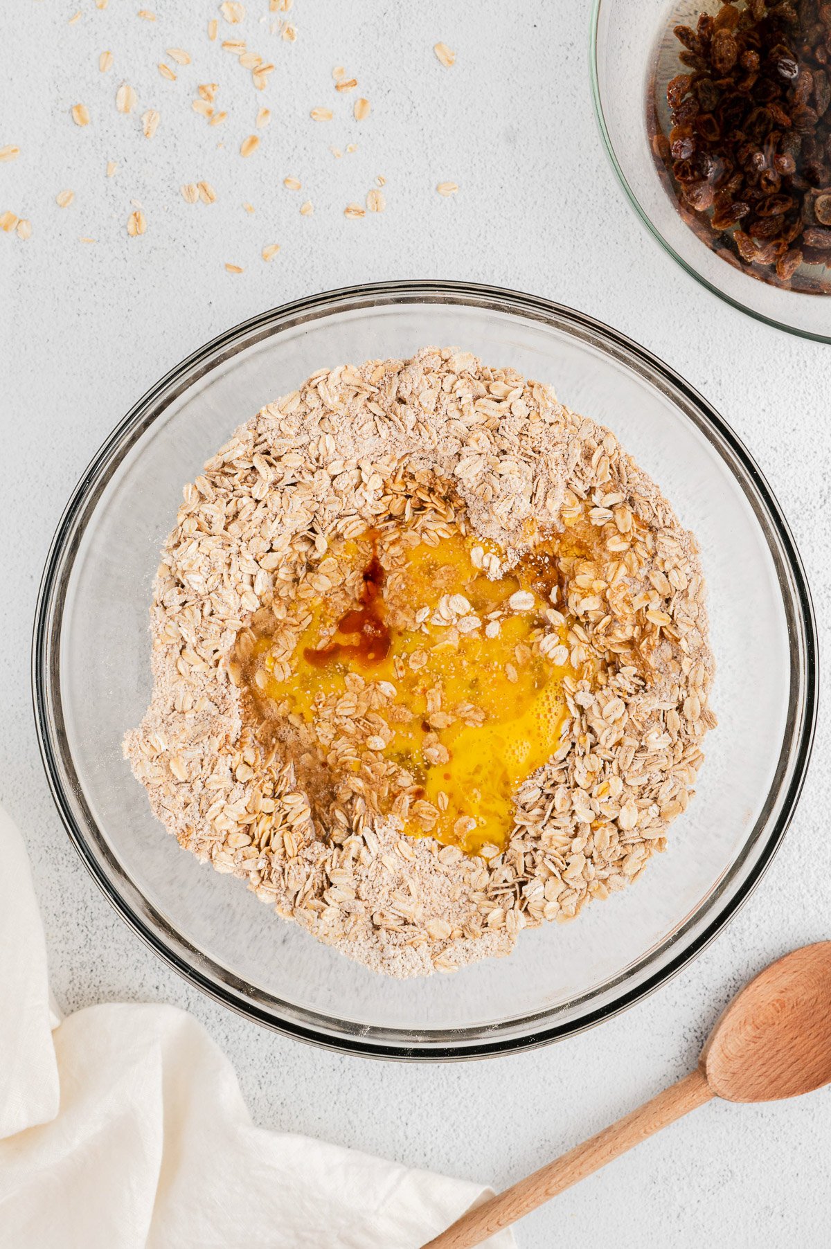 Rolled oats, oat flour, baking soda, baking powder, salt, and cinnamon in a clear bowl on a white background before being mixed for oatmeal raisin cookies