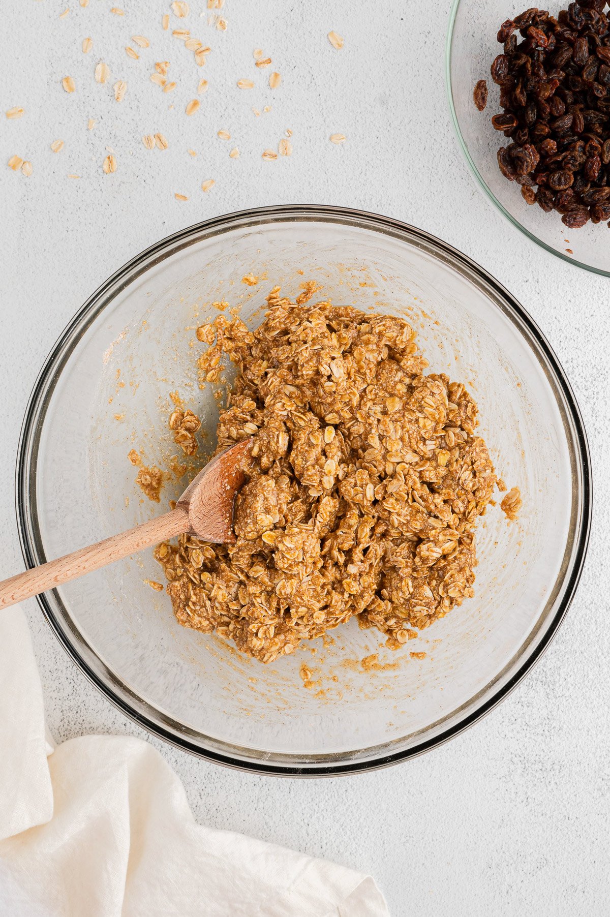Cookie batter for Healthy Oatmeal Raisin Cookies in a clear bowl before adding raisins after maple syrup was added