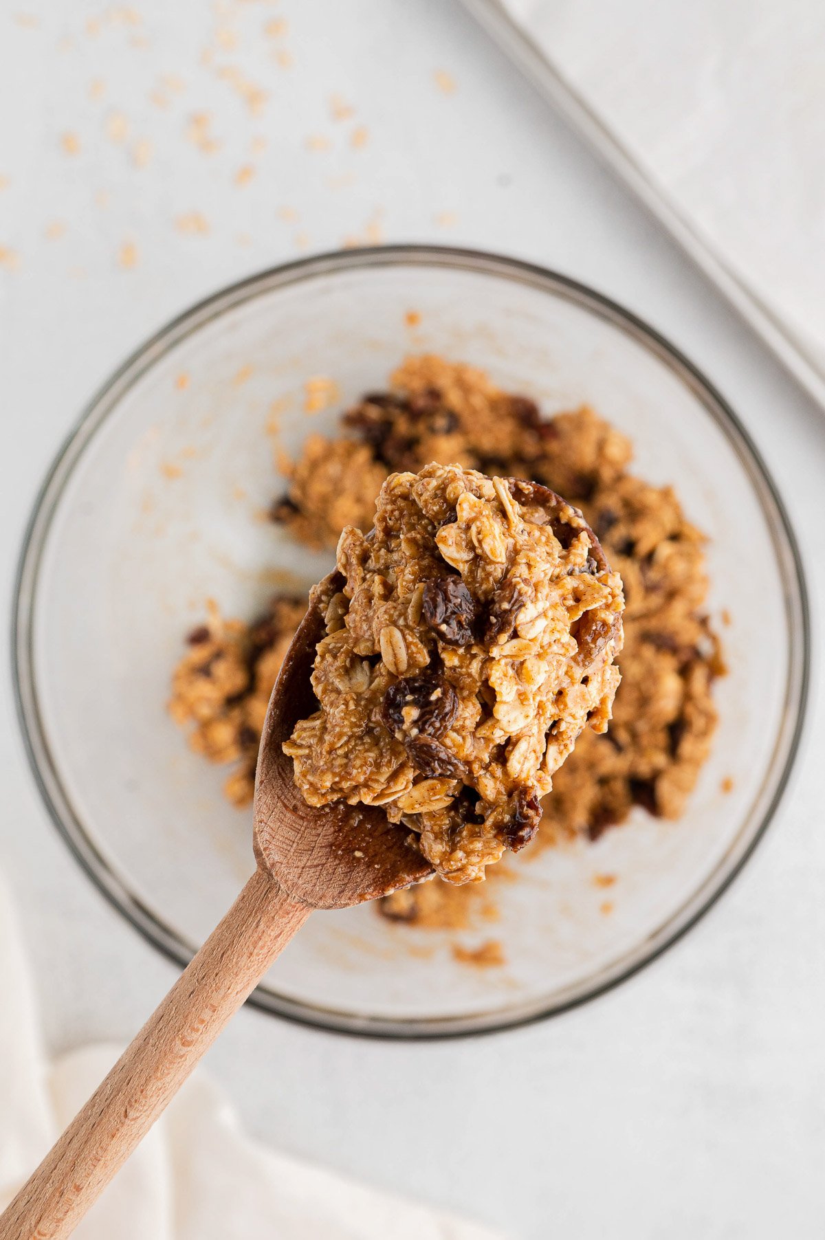 A close up of a wooden spoon with Oatmeal Raisin Cookie Dough on it with the clear bowl in the background