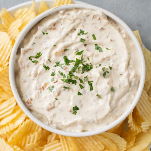 An overhead shot of a bowl of Healthy Onion Dip with potato chips on the side on a grey background