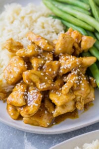 A close up of healthy orange chicken on a white plate with green beans and rice on the side.
