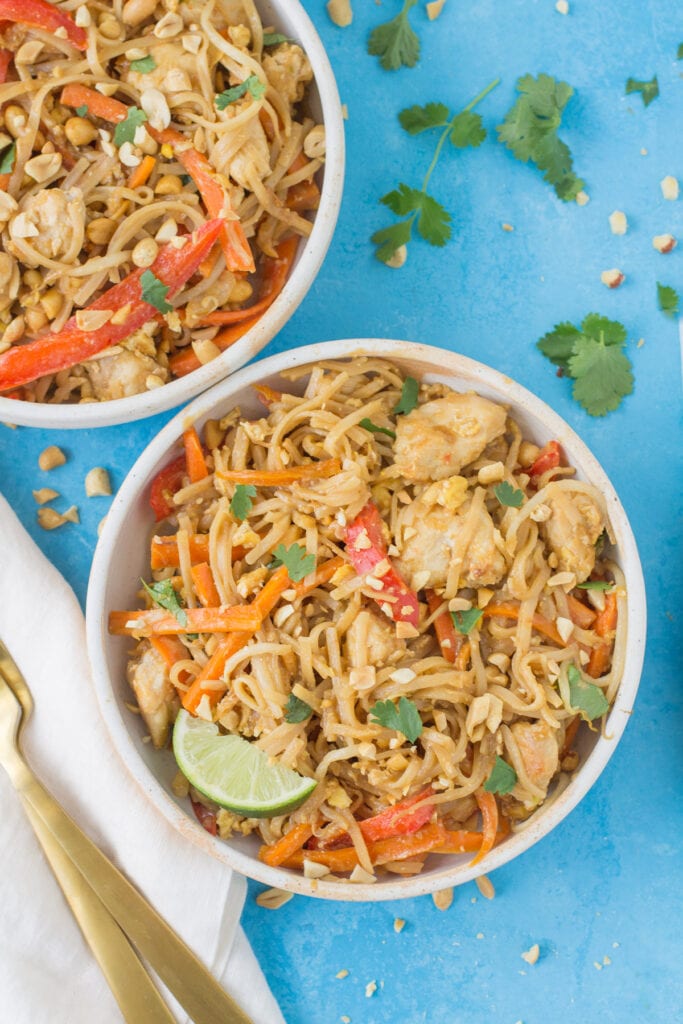Two white bowls filled with Healthy Chicken Pad Thai on a bright blue background