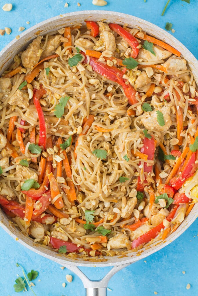 An overhead image of pad thai sauted in a white pan a blue background