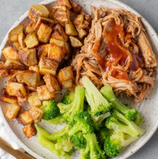 Healthy Crockpot Pulled Pork in a white dish with roasted potatoes and broccoli off to the side