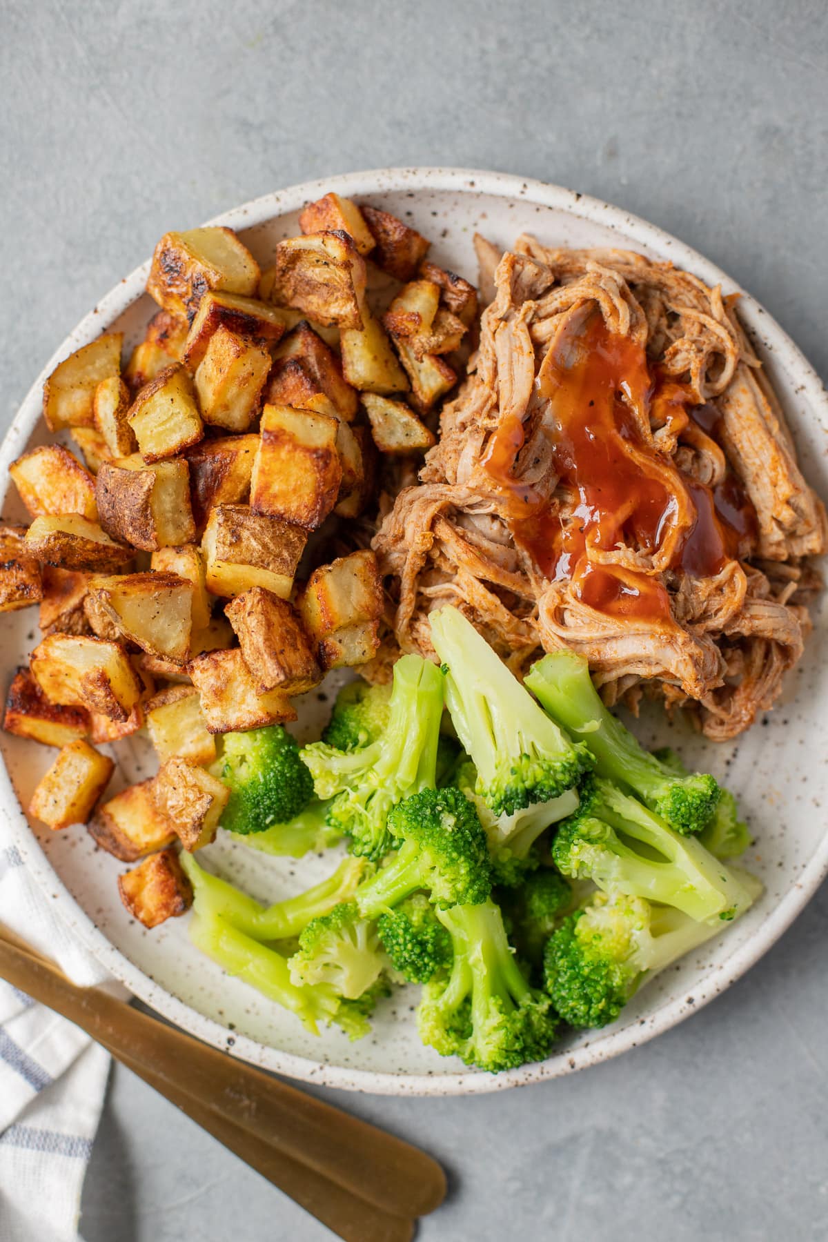 Healthy Crockpot Pulled Pork in a white dish with roasted potatoes and broccoli off to the side