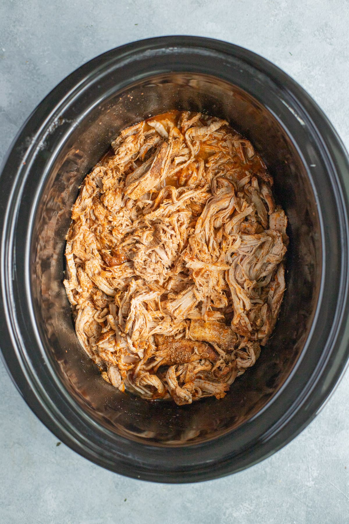 Healthy Crockpot Pulled Pork in a slow cooker base on a grey background