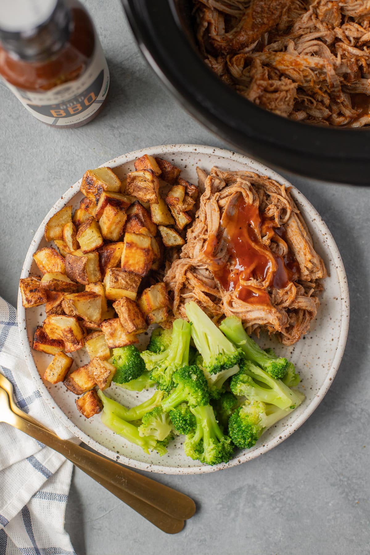 the best slow cooker Pulled Pork in a bowl with potatoes and broccoli with BBQ sauce and a crockpot off to the side