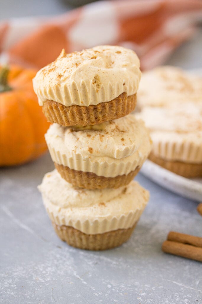 Healthy Pumpkin Cheesecakes stacked on top of one another with a plate of cheesecakes in the background