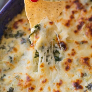 a chip scooping into Healthy Spinach Artichoke Dip, the dip is warm, melty and cheesy