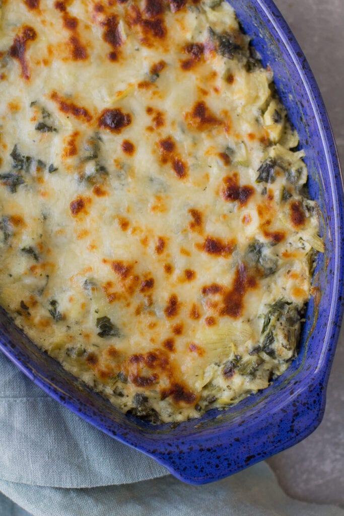 A close up of a blue dish with Healthy Spinach Artichoke Dip in it. No mayo or cream cheese is in the dip