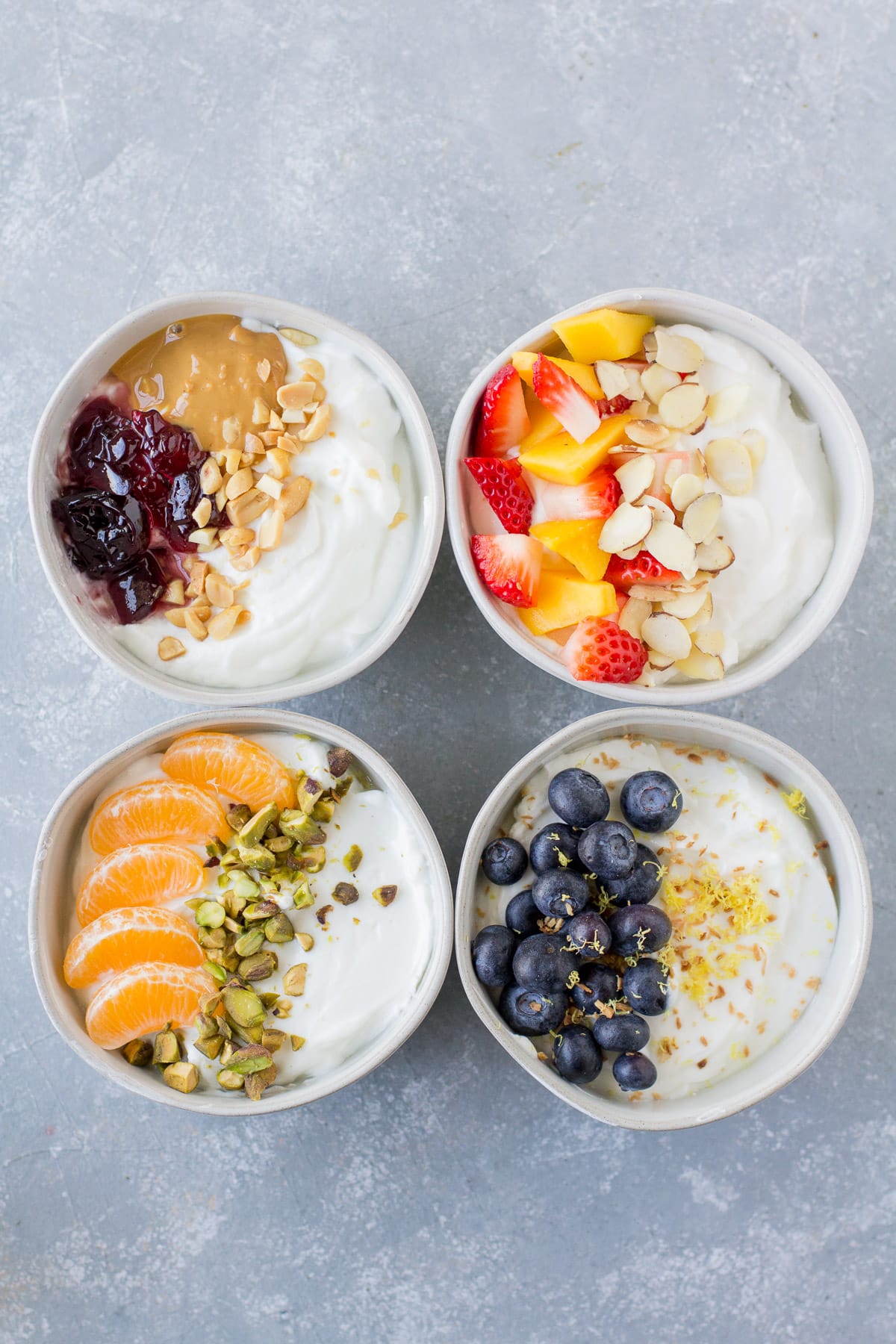 An overhead shot of 4 healthy yogurt bowls on a grey background