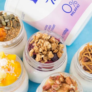 5 Healthy Yogurt Parfaits in glass jars with a carton ofFAGE Yogurt off to the side