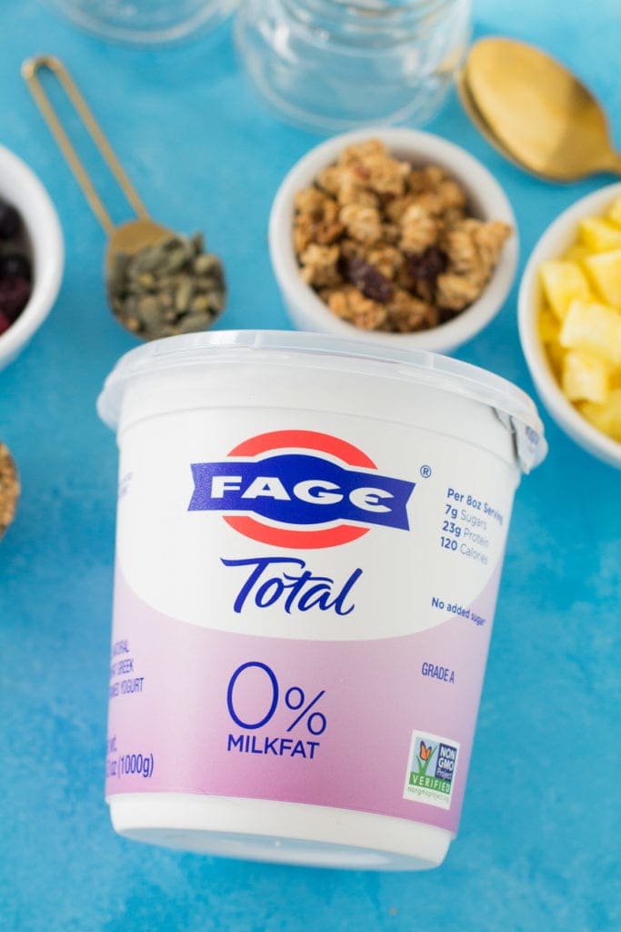 A carton of yogurt surrounded by parfait ingredients + jars.
