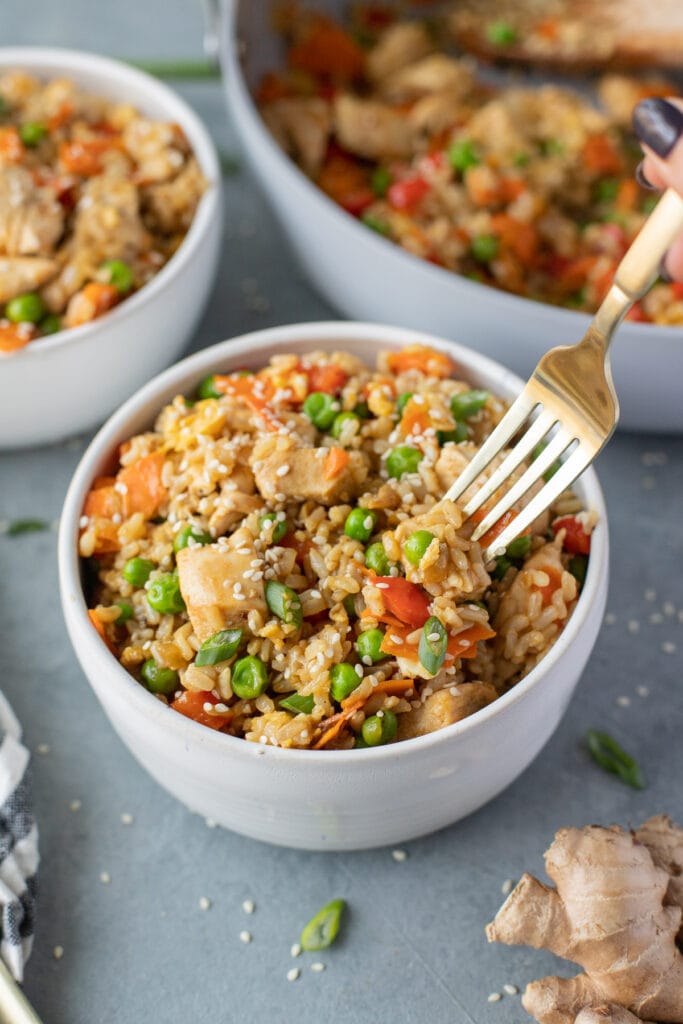 A gold fork taking a bite out a bowl of healthy chicken fried rice.