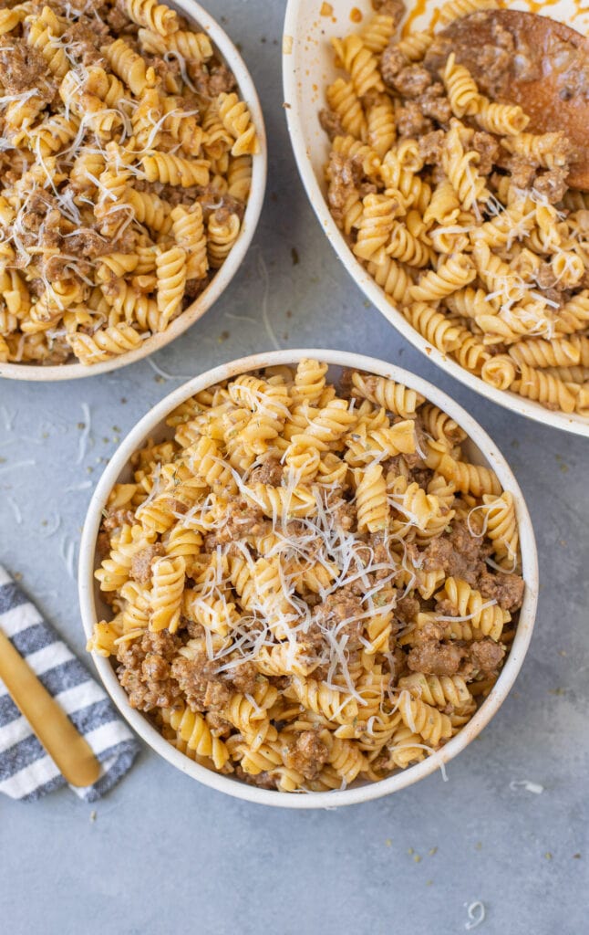 Bowls of homemade hamburger helper recipe with a pan off to the side on a grey background
