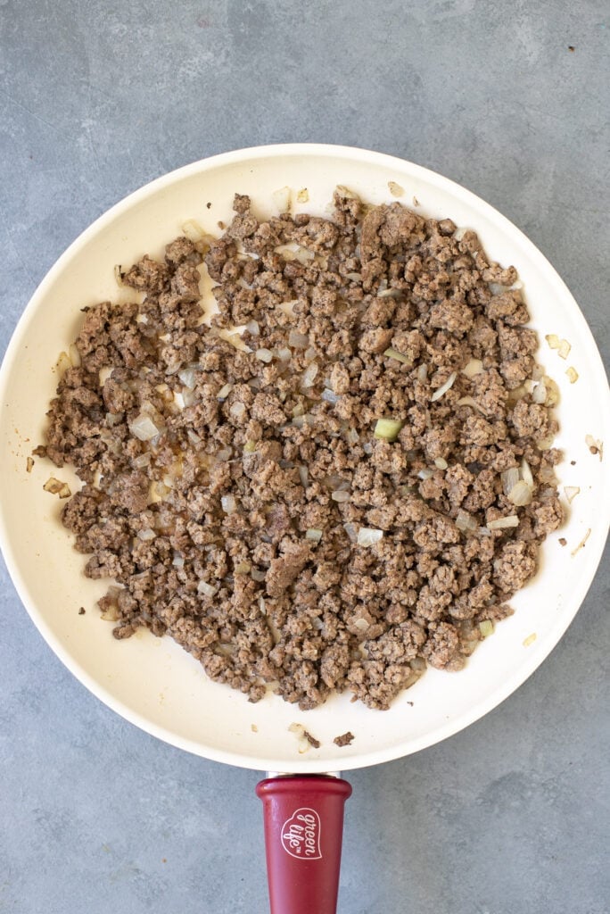 Ground beef and onions browning in a white pan for homemade hamburger helper