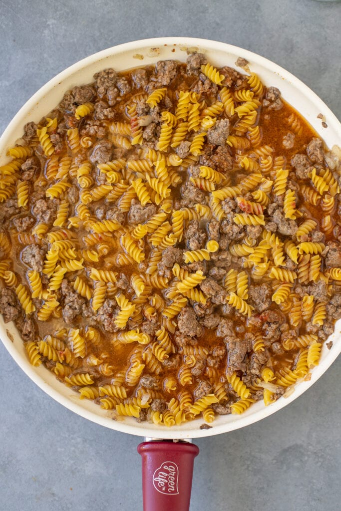 dry pasta, beef and seasonings being stirred together for homemade hamburger helper