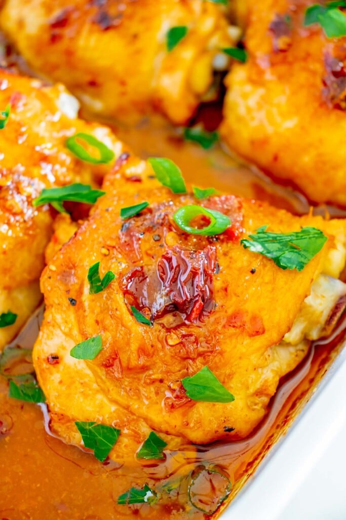 A close up of honey chipotle chicken thigh in a white baking dish with more thighs around it