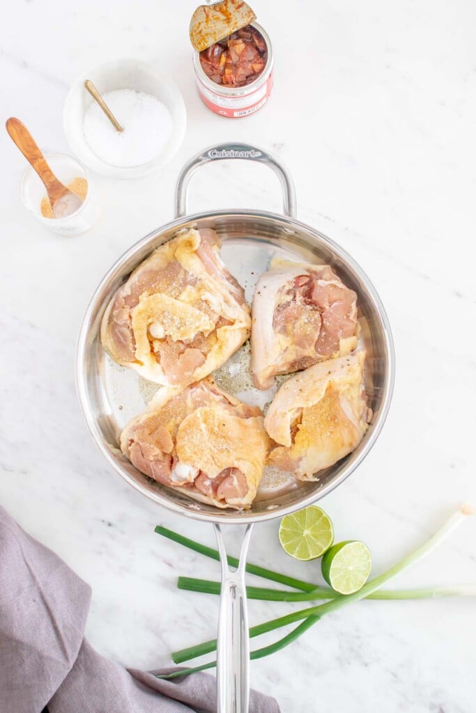 4 chicken thighs in a pan that have been seasoned on a white background before being cooked